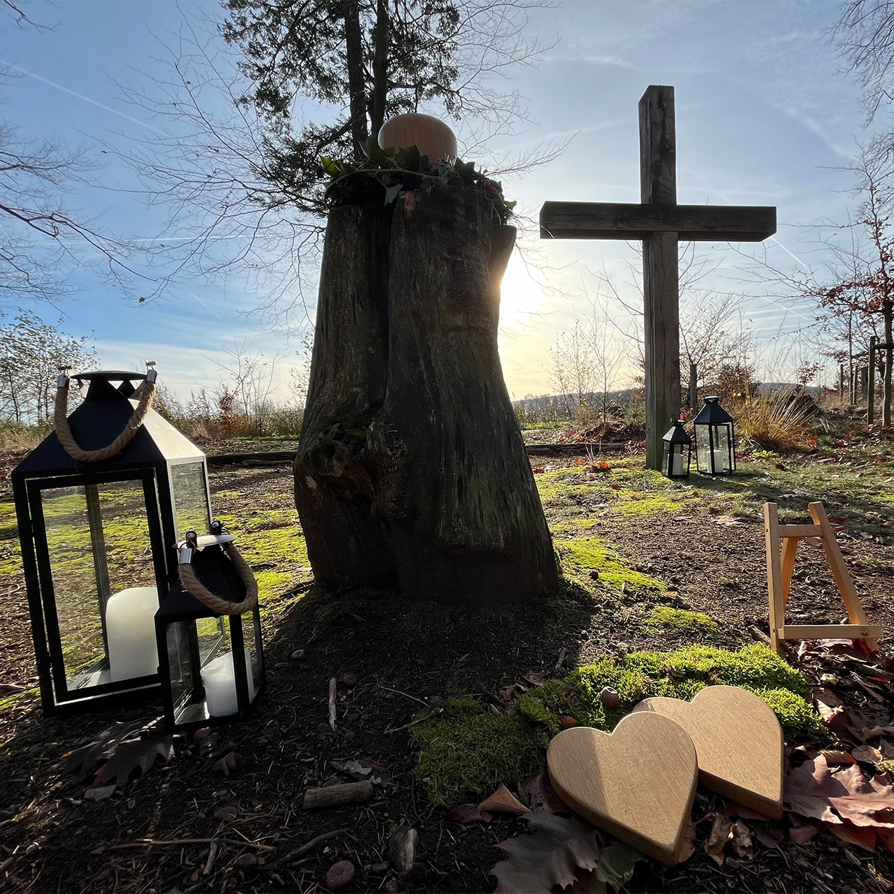 Brennende Kerzen in herbstlicher Natur mit Kreuz – Symbol für Trauer, Erinnerung und Abschied